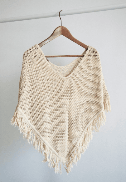 A cream crochet poncho on a hanger